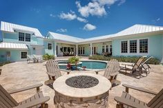 an outdoor fire pit with chairs around it in front of a pool and two large white houses