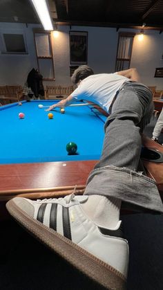 a man is playing pool on a table with his feet propped up in the air