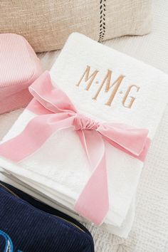 a personalized towel with a pink bow sits on a bed next to a pillow