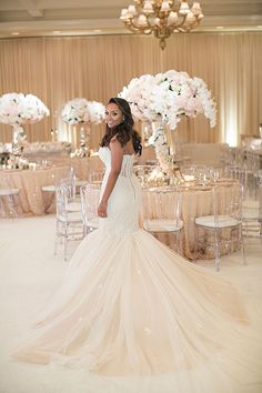 a woman in a wedding dress standing next to a table with chairs and flowers on it