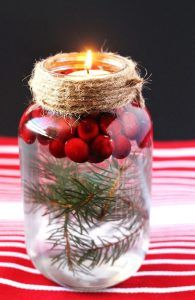 a glass jar filled with red berries and a lit candle sitting on top of a table