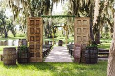 an outdoor ceremony set up with wooden doors and wine barrels on the grass, surrounded by trees