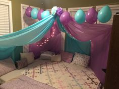 a bed with blue and purple balloons hanging from the ceiling