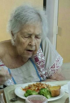 an old woman sitting at a table eating food