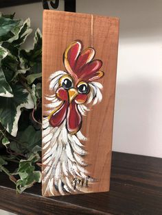 a wooden sign with a rooster painted on it next to a potted green plant