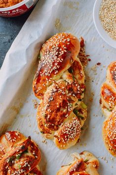 several hot dogs with sesame seeds and other toppings on a sheet of parchment paper