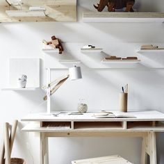 a white desk with wooden shelves on the wall above it and a small stool in front of it