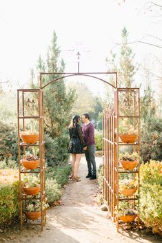 a man and woman standing in front of an arch with potted plants on it