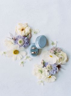 two wedding rings and some flowers on a white surface