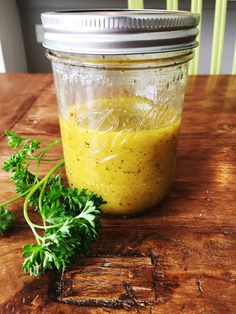 a jar filled with yellow liquid sitting on top of a wooden table next to a sprig of parsley