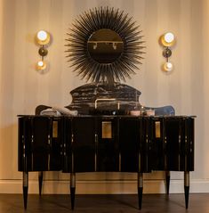 a black and gold sideboard in front of a wall with a sun mirror on it