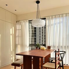 a dining room table and chairs in front of a large window with white drapes