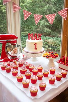 a table topped with lots of cupcakes next to a red and white cake