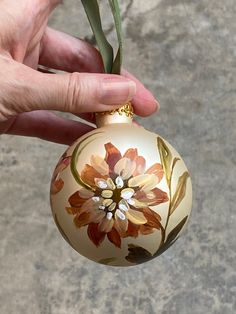 a hand holding a glass ornament with a flower painted on it's side