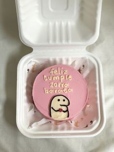 a pink and white cupcake in a plastic container with writing on the lid that says feliz cumple zong bao