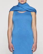 a woman wearing a blue dress with a cowl neck and sleeveless top, standing in front of a white background