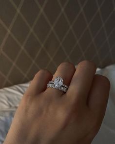 a woman's hand with a diamond ring on top of her finger and the other hand holding an engagement ring