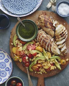 a wooden plate topped with meat and veggies next to bowls of sauces