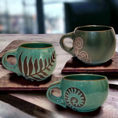 two green coffee mugs sitting on top of a wooden table next to each other