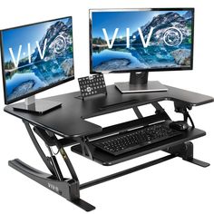 two computer monitors sitting on top of a black stand up desk with keyboard and mouse