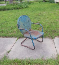 an old blue chair sitting in the middle of a sidewalk next to a grass field