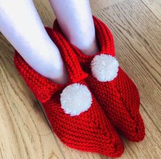 someone is wearing red knitted slippers with white pom - poms