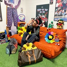 a man sitting on top of an orange couch surrounded by stuffed animals and other items