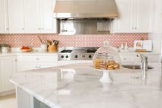 a white kitchen with marble counter tops and stainless steel appliances in the backround