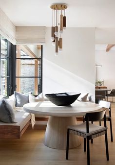 a dining room table with chairs and a bowl on top of it in front of a window