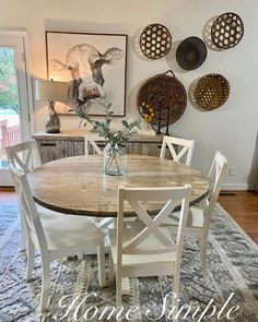 a dining room table with white chairs and pictures on the wall in the back ground