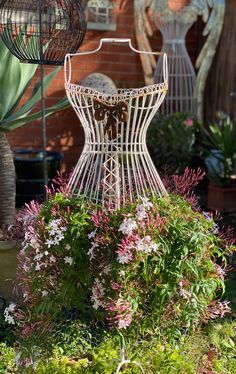 an iron dress form sitting in the middle of some flowers and plants outside on a sunny day