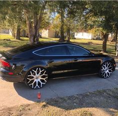 a black car with chrome wheels parked on the side of the road in front of some trees