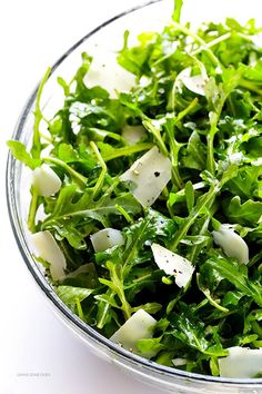 a glass bowl filled with greens and cheese