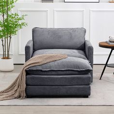 a living room with a chair, ottoman and potted plant on the side table