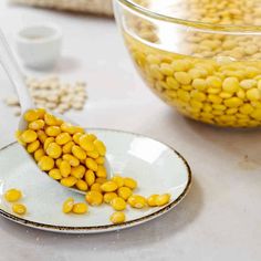 a spoon filled with corn on top of a plate next to a bowl of cereal