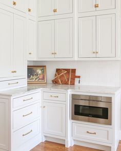 a kitchen with white cabinets and gold handles