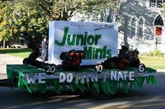 a green and white truck driving down a street next to a tree filled road with people on it