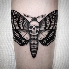 a black and white moth tattoo on the leg, with a skull in the middle