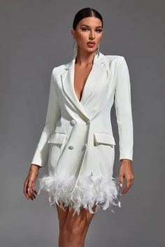 a woman in a white suit with feathers on the skirt and heels, standing against a gray background