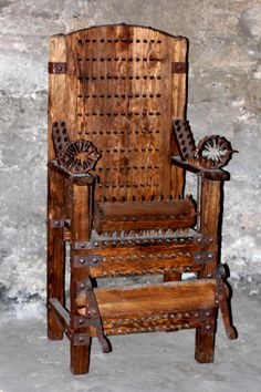 an old wooden chair sitting in front of a stone wall with metal decorations on it