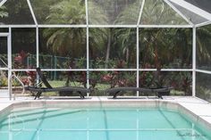 two chaise lounges sitting next to a swimming pool in front of a glass enclosed area