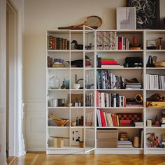 a white bookcase filled with lots of books on top of a hard wood floor