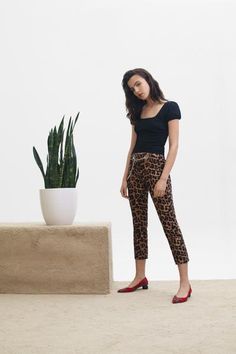 a woman standing next to a potted plant wearing leopard print pants and red shoes