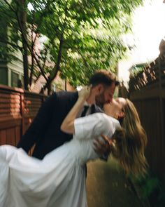 a bride and groom are kissing in front of a fence with their arms around each other