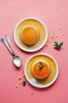 two white plates topped with desserts on top of a pink surface next to spoons