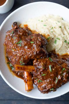 a white plate topped with meat and mashed potatoes next to a cup of gravy