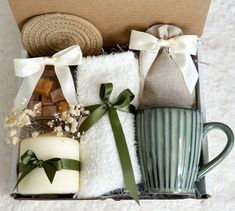 a gift box containing two mugs, a candle and some towels with bows on them