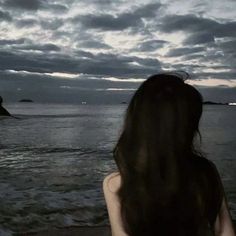 a woman standing on top of a sandy beach next to the ocean at night time