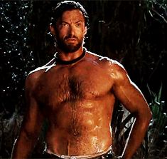 a man without a shirt standing in the woods with his hands on his hips and one hand on his hip