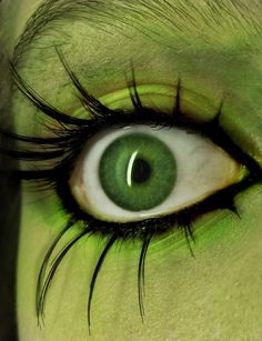 an eye with green eyeshade and long eyelashes, painted to look like a creature's face